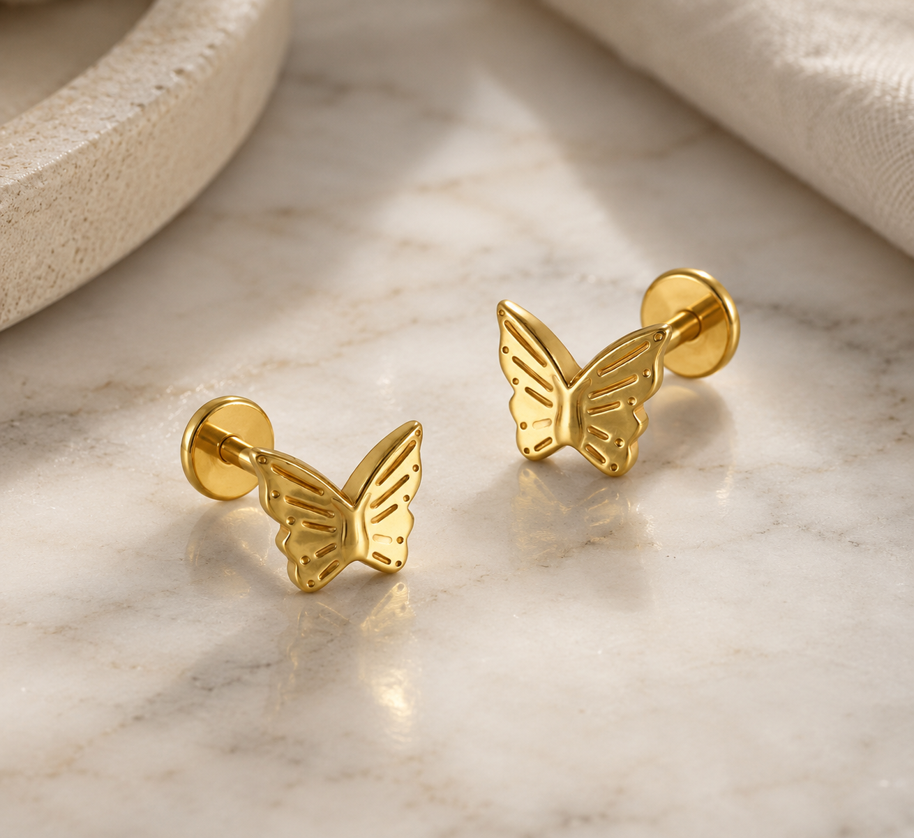Gold titanium butterfly earrings on marble